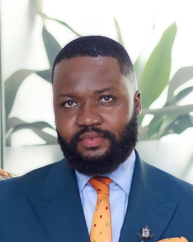 A photo of Ken Akan with a beard wearing a suit and tie.