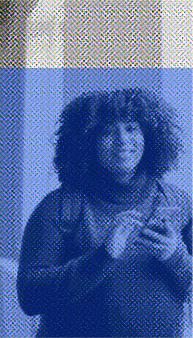 A woman with curly hair standing in front of a blue and white background.